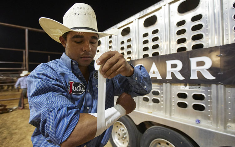 Laramie Mosley wearing a blue shirt taping up his wrist, preparing for the rodeo.